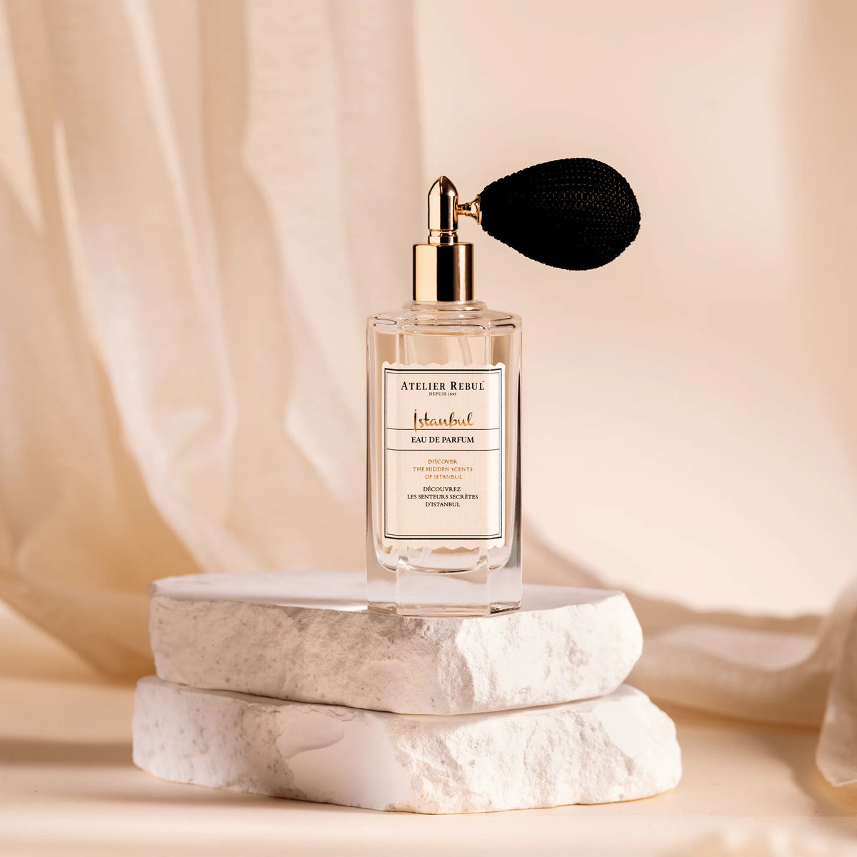 Atelier Rebul Istanbul Eau de Parfum 50 ml mit schwarzem Ballonzerstäuber auf hellen Steinplatten vor cremefarbenem Stoff.