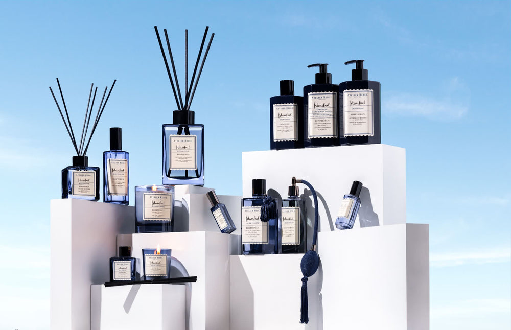 Edle Duftprodukte von Atelier Rebul aus der Bosphorus-Kollektion, stilvoll arrangiert vor blauem Himmel. Luxuriöse Raumdüfte, Parfums und Pflegeprodukte in eleganten blauen Glasflaschen.