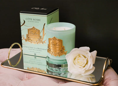 gruene duftkerze mit goldener inschrift, gruene verpackung und weisse single rose auf goldenem serviertablett. seitenansicht.