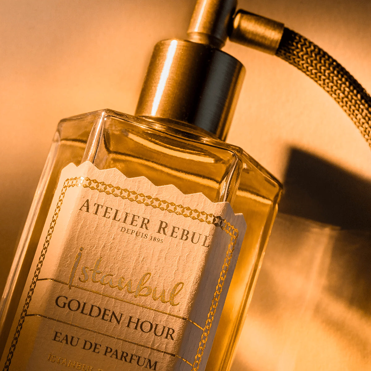 Nahaufnahme des Atelier Rebul Istanbul Golden Hour Flakons mit verziertem Etikett und bronzefarbenem Sprühkopf in warmem, goldenem Licht.