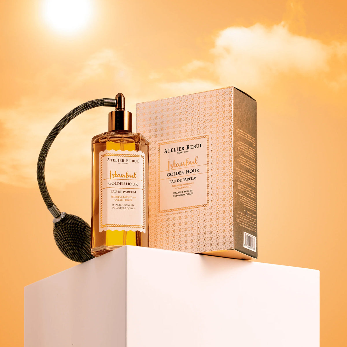 Atelier Rebul Istanbul Golden Hour Eau de Parfum mit Ballzerstäuber und goldgemusterter Verpackung auf weißem Podest vor goldgelbem Hintergrund.
