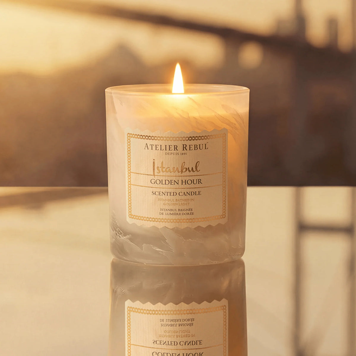 Brennende Atelier Rebul Istanbul Golden Hour Duftkerze 210 g im cremefarbenen Glas auf einer spiegelnden Oberfläche.