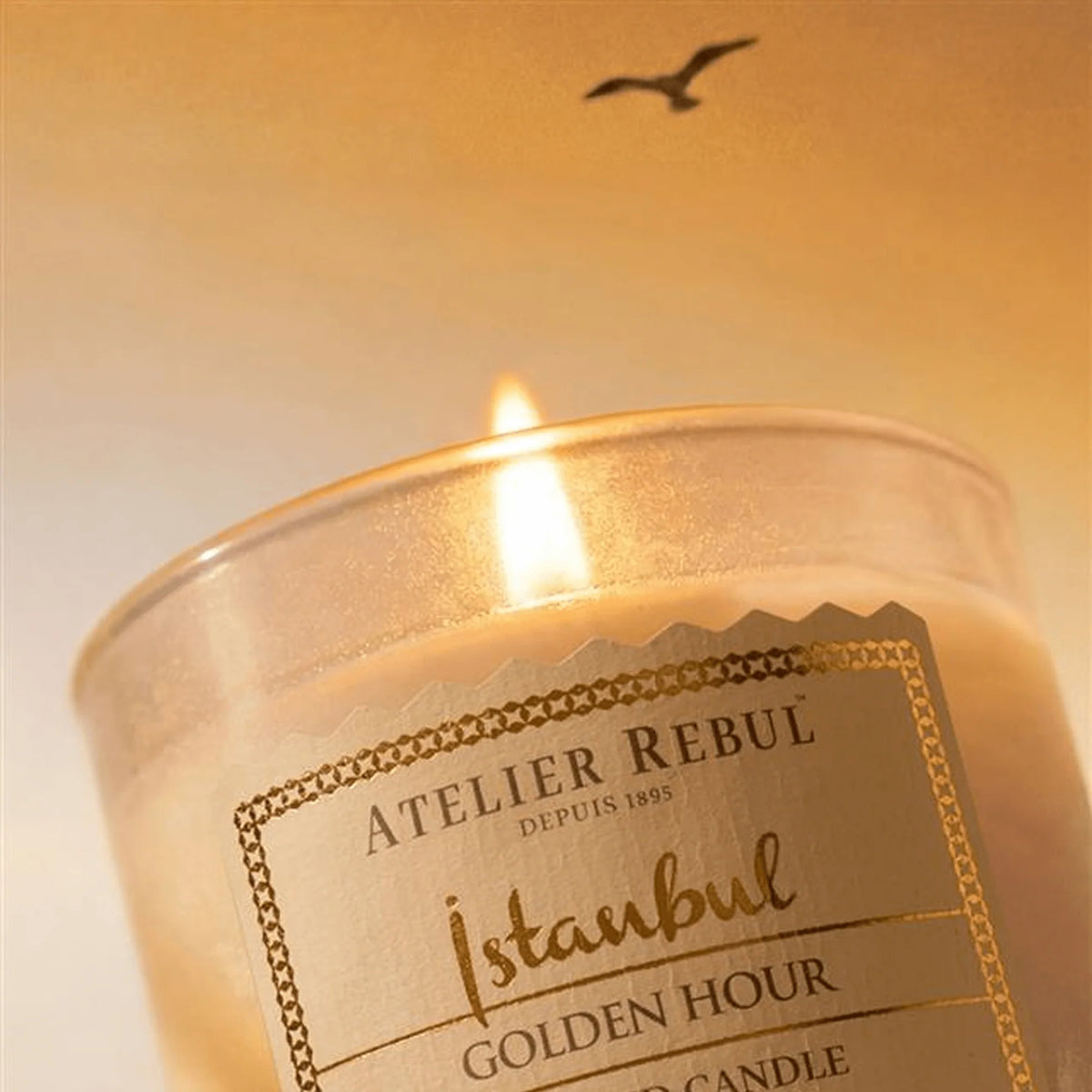 Nahaufnahme der brennenden Atelier Rebul Istanbul Golden Hour Duftkerze 210 g mit Etikett und Flamme im goldenen Licht.