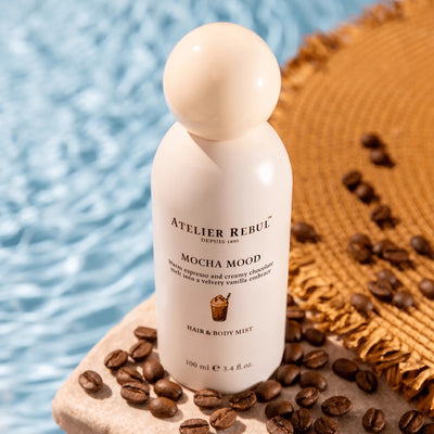 Atelier Rebul Mocha Mood Haar- und Körperspray steht zwischen Kaffeebohnen am Poolrand neben einer geflochtenen Matte.