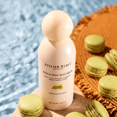 Atelier Rebul Pistachio Macaron Haar- und Körperspray steht zwischen grünen Macarons am Poolrand neben einer geflochtenen Matte.