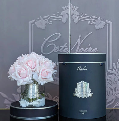 french pink rosen in hellem glas neben dunkler geschenkbox.