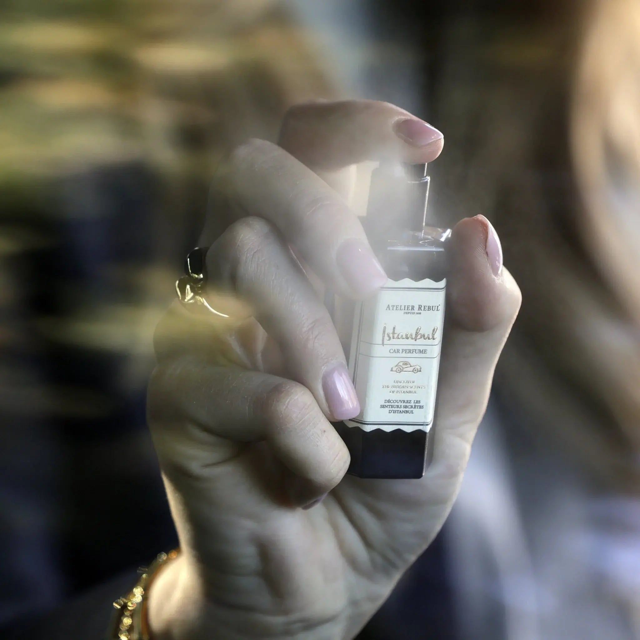 Eine elegante Hand mit goldener Armspange sprüht das Istanbul Auto Parfum ins Licht.