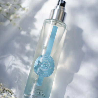 liegende durchsichtige glasspruehflasche eau fraiche baumwoll moschus auf einem weissen tisch mit schleierkraut