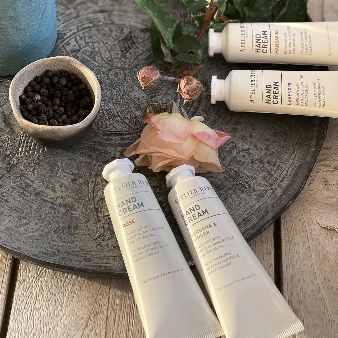 auf dekorativer steinplatte mit rosen und einer schale mit pfefferkoerner liegen 4 verschiedene kleine handcreme  