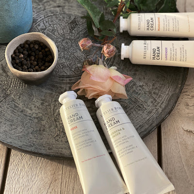 auf dekorativer steinplatte mit rosen und einer schale mit pfefferkoerner liegen 4 verschiedene kleine handcreme  