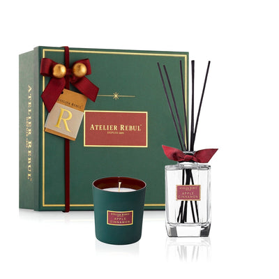 weihnachtlich gruene geschenkverpackung mit roter schleife und goldenen gloeckchen vor duftkerze und dutfstaebchen.