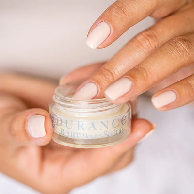 lackierte frauenhaende halten die durance den geoeffneten lippenbuttertigel hintergrund rose