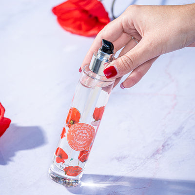 eine hand haelt leichtschraeg die runde glaspumpflasche schoene mohnblume hintergrund weiss mit mohnblumen 