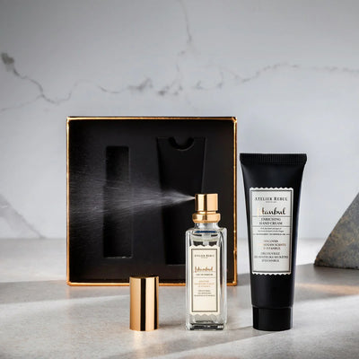 geoeffnete box stehend im hintergrund. davor handcreme und parfum, welches einen spruehstoss abgibt.