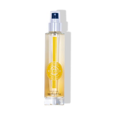 durchsichtige runde glasflasche eau fraiche sinnliches monoi mit silbernen spruehkopf vor weissem hintergrund