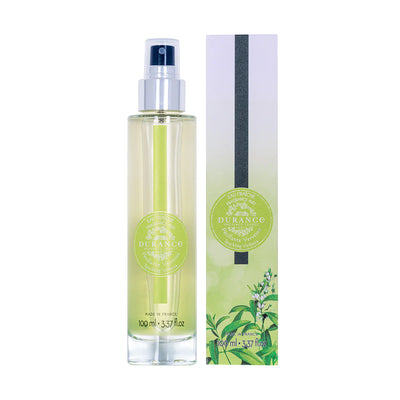 durchsichtige runde glasflasche eau fraiche prickelnde verbene mit silbernen spruehkopf und verpackung vor weissem 